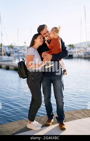 Beautiful family is hugging each other and enjoying a sunny day on a boat pier by the sea Stock Photo