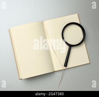 Paper notebook with blank white sheets and a black magnifier on a gray background Stock Photo