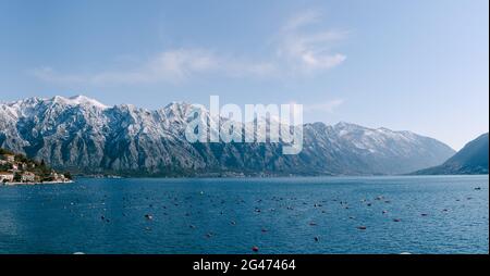 Snow-capped mountain peaks in Kotor Bay, Montenegro, above the city of Dobrota. An assiable and fish farm in the sea. Stock Photo