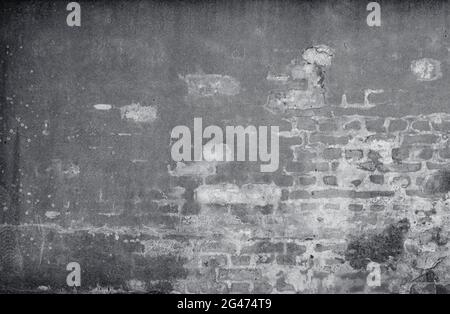 Front view of an old, dirty, damaged&plastered wall. Plaster is partly peeled off revealing old bricks. Full frame textured background in black&white. Stock Photo