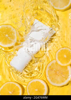 Cosmetic tube in water,lemon slices,yellow bg Stock Photo