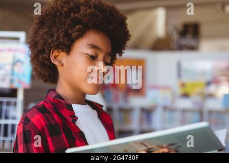 Smiling african american schoolboy reading book standing in school library Stock Photo