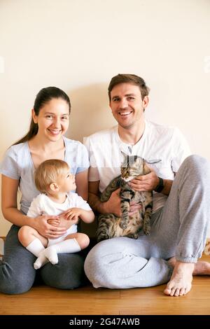 Mom holds a little girl on her lap and dad holds a tabby cat Stock Photo