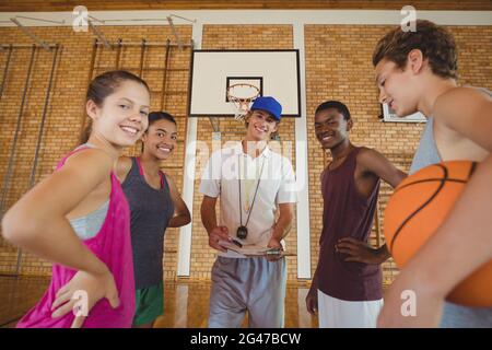 Smiling high school kids and their coach standing in the basketball court Stock Photo