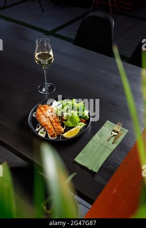One piece of baked salmon grilled pepper lemon and salt on a black plate with lettuce leaves on a stone background Stock Photo