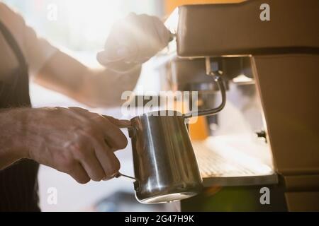 Mid section of waiter pouring milk in jug from coffee machine Stock Photo