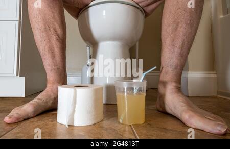 Close up of legs of senior caucasian adult sitting on toilet preparing for colonoscopy with medication Stock Photo