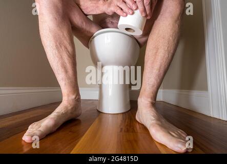 Close up of legs of senior caucasian adult sitting on toilet holding paper for colonoscopy prep Stock Photo