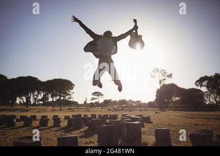Happy man holding guitar while jumping against clear sky Stock Photo