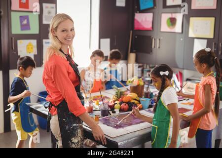 Portrait of smiling teacher assisting schoolkids in drawing class Stock Photo