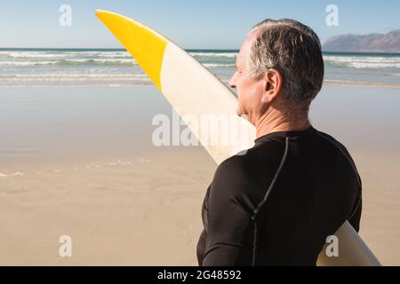 Rear view of senior man carrying surfboard Stock Photo