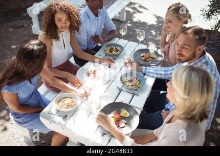 Happy friends interacting with each other while having meal Stock Photo