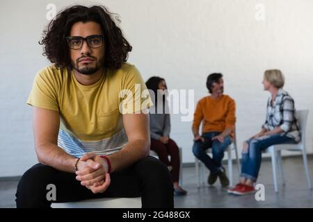 Portrait of man sitting on chair with friends discussing in background Stock Photo