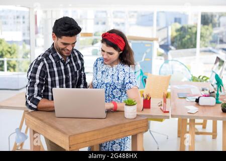 Male and female executives discussing over laptop at desk Stock Photo