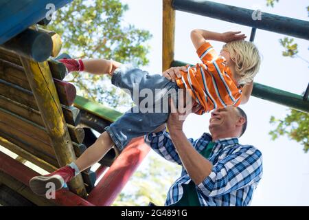 Low angle view of father assisting son in playing on jungle gym Stock Photo