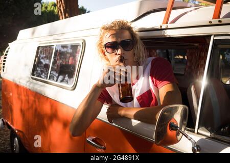 Man drinking beer while leaning on camper van window Stock Photo