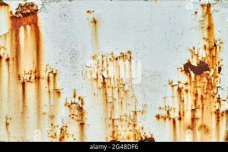 Patches of rust stain a white painted metal surface. The pain cracked to reveal the metal underneath. Stock Photo