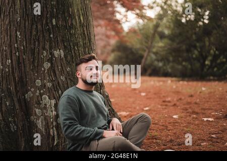 Young man sitting next to a tree in a park Stock Photo