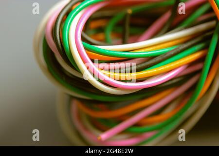 A bundle of multicolored electrical, car, computer, telephone wires twisted together background. Orange, green, pink, white cables on grey background Stock Photo