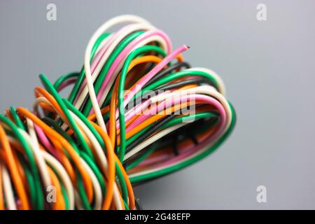 A bundle of multicolored electrical, car, computer, telephone wires twisted together background. Orange, green, pink, white cables on grey background Stock Photo