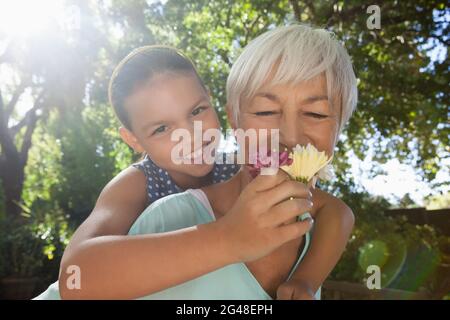 Grandmother smelling flowers while piggybacking granddaughter Stock Photo