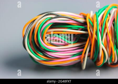 A bundle of multicolored electrical, car, computer, telephone wires twisted together background. Orange, green, pink, white cables on grey background Stock Photo