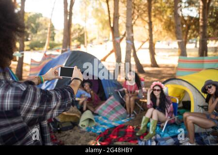 Man photographing smiling friends through mobile phone Stock Photo