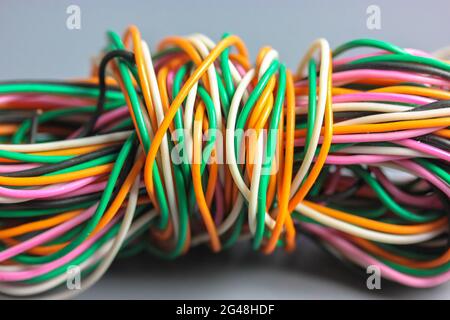 A bundle of multicolored electrical, car, computer, telephone wires twisted together background. Orange, green, pink, white cables on grey background Stock Photo