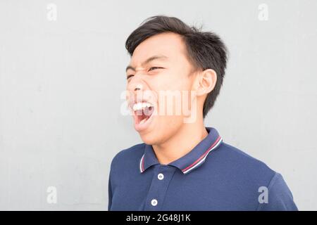 Indonesian guy with a blue t-shirt madly screaming on a white background Stock Photo