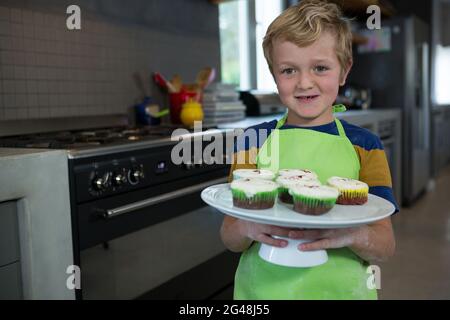 Portrait of boy holding plate with cupcakes Stock Photo