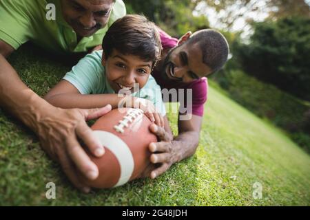 Happy boy playing rugby with father and grandfather at park Stock Photo