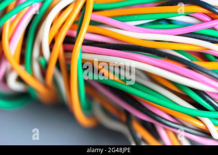 A bundle of multicolored electrical, car, computer, telephone wires twisted together background. Orange, green, pink, white cables on grey background Stock Photo