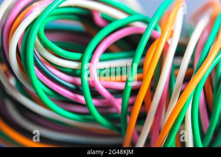 A bundle of multicolored electrical, car, computer, telephone wires twisted together background. Orange, green, pink, white cables on grey background Stock Photo