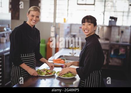 Smiling female chefs with fresh food in plates on kitchen counter Stock Photo