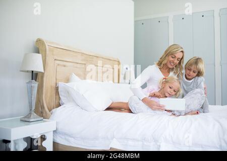 Mother and kids using digital tablet on bed in bed room Stock Photo