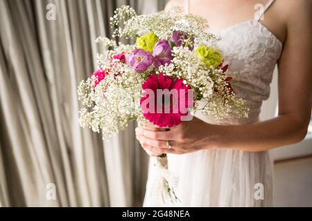 Midsection of bride in wedding dress holding bouquet at home Stock Photo