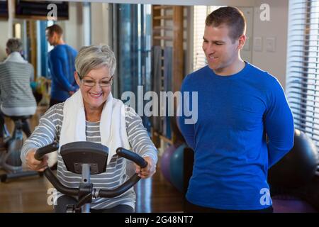 Physiotherapist assisting senior woman in performing exercise on exercise bike Stock Photo