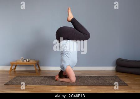 Pregnant woman doing exercises standing in a yoga pose headstand on her head. Stock Photo
