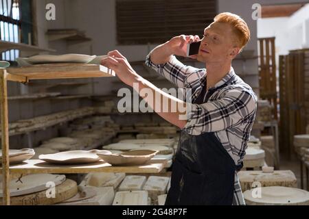 Male potter taking on mobile phone while working Stock Photo