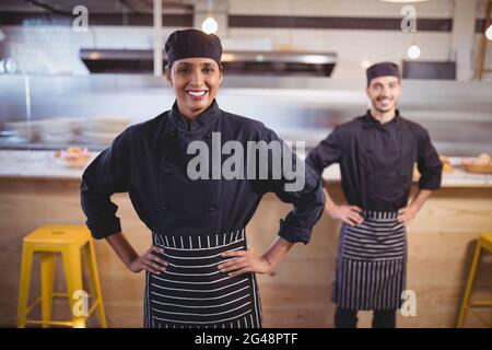 Portrait of smiling young wait staff standing with hands on hip against counter Stock Photo