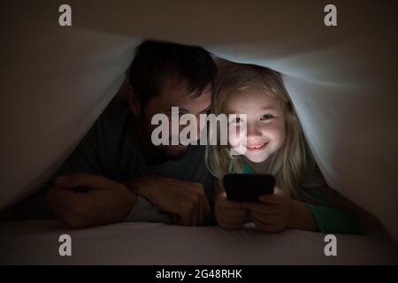 Father and daughter lying under blanket and using mobilephone Stock Photo