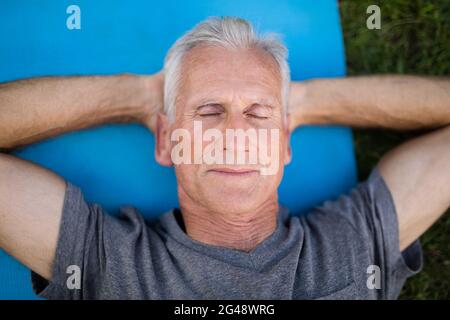 Senior man resting with closed eyes on mat at park Stock Photo