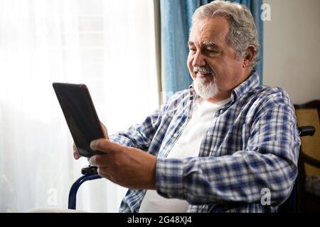 Smiling senior man using digital tablet by sitting on wheelchair Stock Photo