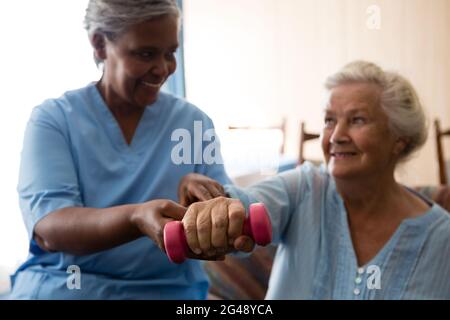 Nurse helping senior woman in lifting dumbell Stock Photo