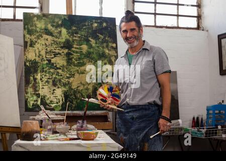 Portrait of confident man standing with palette and paintbrushes Stock Photo