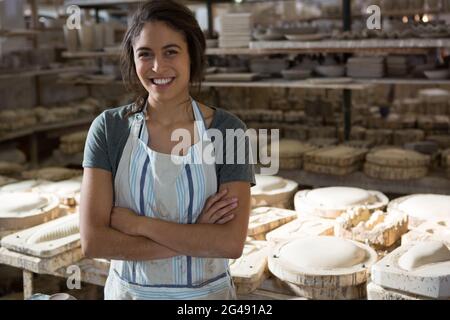 Confident female potter standing with arms crossed in pottery workshop ...