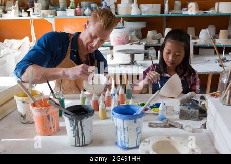 Male potter and girl painting bowl in pottery workshop Stock Photo - Alamy