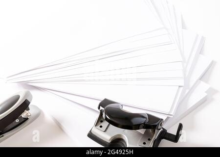 Photograph of some fan-shaped sheets of paper, a stapler and a hole punch for sheets of paper on a white background.The photo has free space to put te Stock Photo