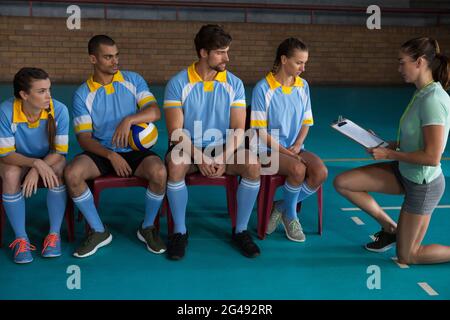 Coach discussing with volleyball players sitting on chairs Stock Photo