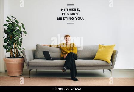 Positive female sitting on sofa in office lobby. Confident entrepreneur sitting in lobby. Stock Photo